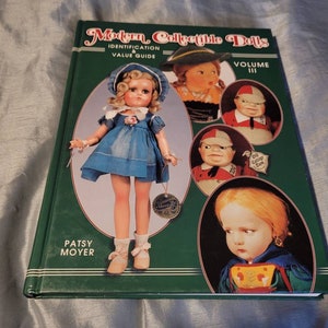 May include: A green book titled "Modern Collectible Dolls Identification & Value Guide Volume III" with a picture of a doll on the cover. The doll is wearing a blue dress and white shoes. The book also features other dolls on the cover.