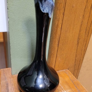 May include: A black ceramic vase with a long, slender neck and a bulbous base. The vase has a blue and white glaze on the top of the neck.
