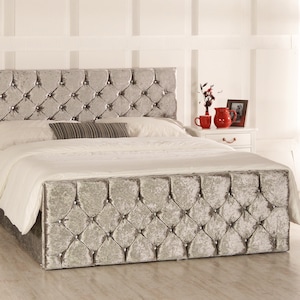 May include: A silver velvet bed frame with a tufted headboard and footboard. The bed frame has a diamond-shaped pattern and is accented with crystal-like buttons.