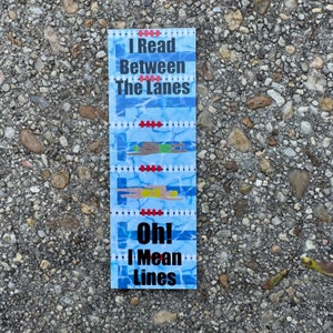 May include: A blue and white bookmark with a swimming pool design. It says "I Read Between The Lanes Oh! I Mean Lines".