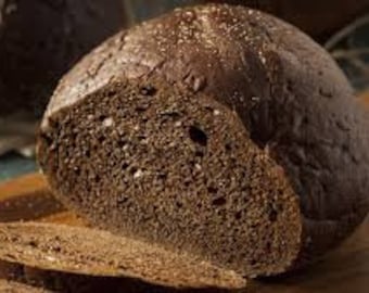 Könnte beinhalten: Ein Laib dunkelbraunes Brot, halbiert, zeigt eine dichte, krümelige Textur. Das Brot liegt auf einem Holzbrett.