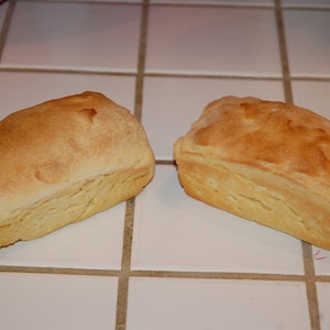 May include: Two golden brown loaves of bread on a white tiled surface.