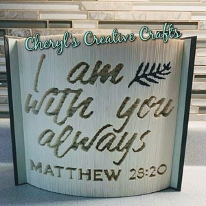 Puede incluir: Un libro blanco con las palabras "Yo estoy contigo siempre" y "Mateo 28:20" en letras negras. El libro está doblado en un diseño 3D con una forma de hoja en el lado derecho. El libro está titulado "Cheryl's Creative Crafts" en la parte superior.