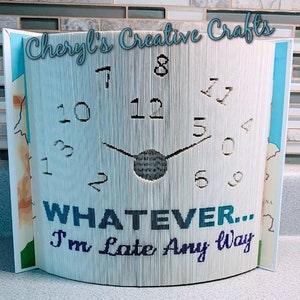 May include: A handmade book clock with the text "WHATEVER... I'm Late Any Way." The clock face is created by folding the pages of a book to form the numbers and clock hands. The words "Cheryl's Creative Crafts" are at the top.