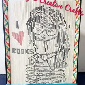 May include: A book art sculpture with a black and white image of a woman with glasses and the text "I love you more" on a white background. The sculpture is framed with a colorful plaid fabric and a turquoise ribbon.