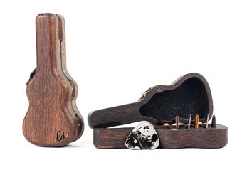 May include: Two dark brown wooden guitar-shaped cases. One case stands vertically, closed, with the letters Ed engraved on the front. The second case lies open horizontally, revealing a black interior lining, holding several guitar picks inside.