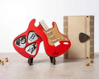 May include: Two red electric guitar shaped photo frames with a wood grain finish. The frame on the left has three guitar pick shaped photo slots. The frame on the right has the name "Sam" written on it. Both frames are on small wooden stands.
