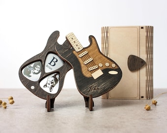 May include: Two wooden guitar-shaped boxes with a pick holder and a stand. The box on the left has the name "Brian" and the box on the right has the name "John".