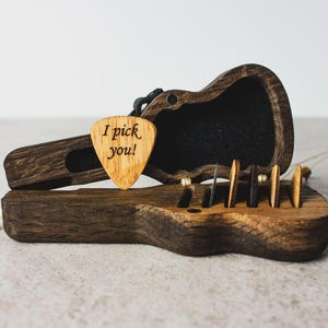 Könnte beinhalten: Eine Gitarre aus Holz mit einem Plektrum im Inneren. Das Plektrum ist aus Holz und hat die Worte "I pick you!" eingraviert.