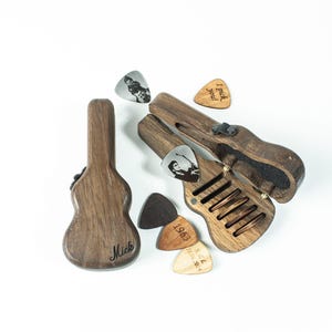 Könnte beinhalten: Ein hölzerner Gitarren-Plektrumhalter in Gitarrenform mit einem Schlitz zum Aufbewahren von Plektrums. Der Halter ist geöffnet und zeigt eine Auswahl an Plektrums, darunter eines mit dem Text "I pick you".