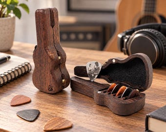 May include: Two dark brown wooden guitar-shaped cases, one standing upright and one open, revealing a black interior with three guitar picks. A white pick with a black and white photo print rests on the open case, with three additional picks placed on the surface.