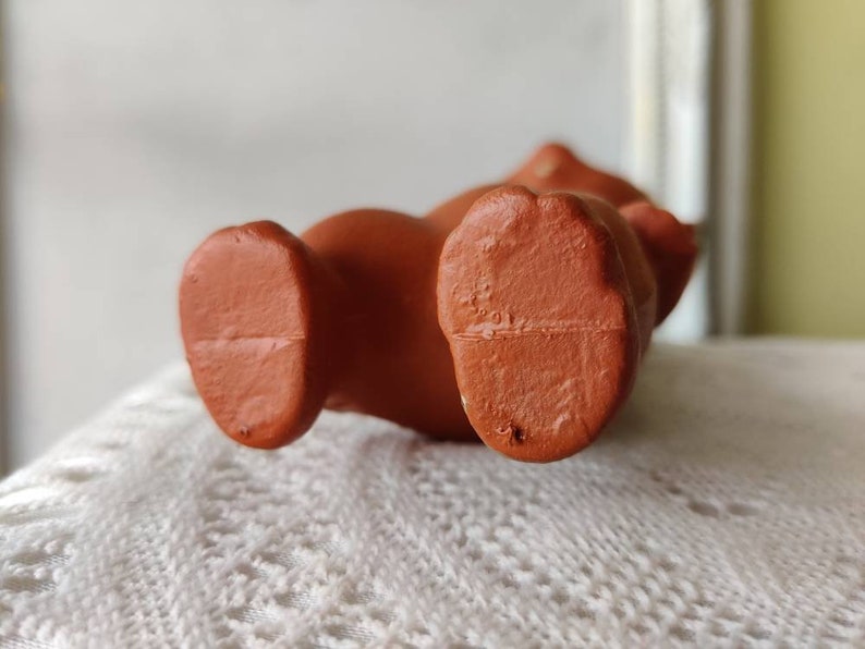 May include: Close-up of the bottom of a brown rubber toy. The toy has two feet and a flat bottom.