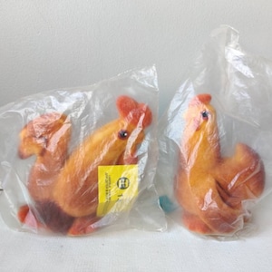 Peut inclure: Deux figurines de coq en peluche marron et orange dans un emballage en plastique transparent. Le coq de gauche porte une étiquette jaune avec le texte "Lassie Craft, Made in West Germany".