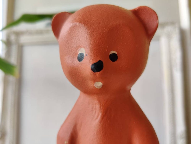 May include: A terracotta-coloured ceramic bear figurine with black painted eyes and a black nose. The bear has a white painted mouth and a slightly surprised expression.