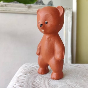 May include: A terracotta brown ceramic bear figurine with black eyes and a simple design. The bear is standing upright with its arms at its sides.