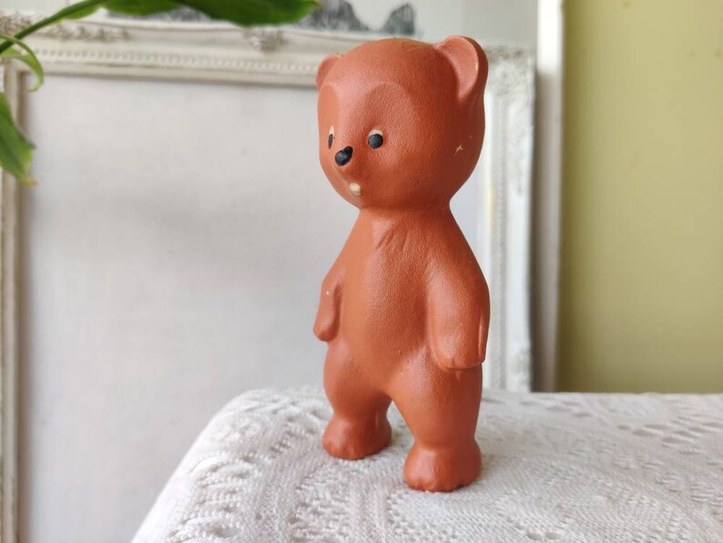 May include: A terracotta brown ceramic bear figurine with black eyes and a simple design. The bear is standing upright with its arms at its sides.