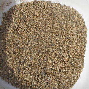 May include: A close-up of a bowl filled with small, light brown and beige gravel. The gravel is uniform in size and appears to be dry.