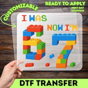 May include: A colorful DTF transfer featuring the text "I WAS NOW I'M 67" constructed from toy building blocks. The design includes the words "CUSTOMIZABLE" and "DTF TRANSFER".