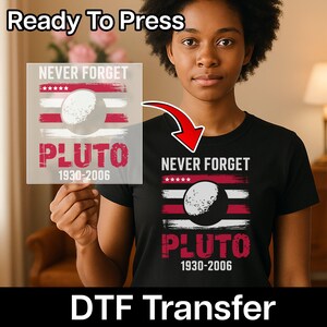 May include: A black t-shirt and a DTF transfer featuring a design with the text "NEVER FORGET PLUTO 1930-2006". The design includes a graphic of Pluto and a flag-like background with red and white stripes. The words "Ready To Press" and "DTF Transfer" are also visible.
