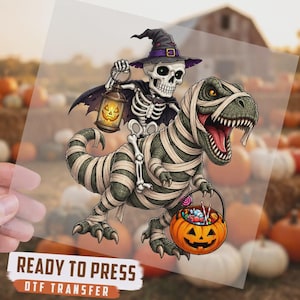 May include: A DTF transfer sheet featuring a cartoon skeleton wearing a purple witch hat and cape, holding a glowing jack-o'-lantern lantern, riding a green mummy-wrapped T-Rex dinosaur that carries a pumpkin bucket filled with candy.