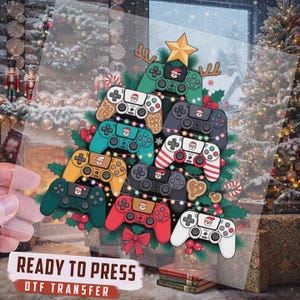 May include: A clear DTF transfer sheet featuring a Christmas tree design composed of various colorful video game controllers. Each controller is decorated with a small Santa Claus icon. The design includes a yellow star topper and string lights.