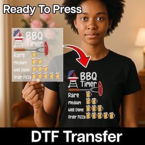 May include: Black t-shirt with a BBQ Timer graphic. The design includes a grill, a meat fork, and a sausage, with text indicating levels of doneness and beer mugs. The words "Ready To Press" and "DTF Transfer" are also visible.