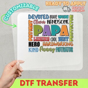 May include: A DTF transfer with the word "PAPA" in large, colorful letters, surrounded by words like "Devoted," "Brave," and "Hero." The design is customizable and ready to apply. The image also includes the text "Ready to Apply" and "Next Day Shipping."