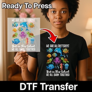 May include: Black t-shirt with a colourful aquatic design featuring a dolphin, fish, octopus, seahorse, jellyfish, and turtles. The text "WE ARE ALL DIFFERENT But in This School WE ALL SWIM TOGETHER" is printed on the shirt. The words "Ready To Press" and "DTF Transfer" are also visible.