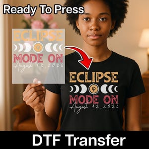 May include: Black t-shirt with a graphic design that says "ECLIPSE MODE ON August 12, 2026" in a retro style. The design includes crescent moon shapes and a sun. The words "Ready To Press" and "DTF Transfer" are also visible.