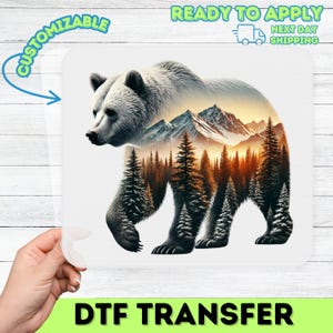 May include: A white bear illustration with a mountain and forest scene inside its silhouette. The image is on a white background with the words "CUSTOMIZABLE", "READY TO APPLY", and "DTF TRANSFER".