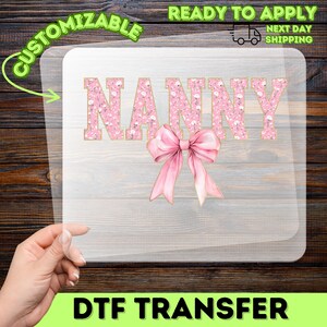 May include: A DTF transfer featuring the word "NANNY" in pink floral print with gold trim, and a pink bow. The transfer is customizable and ready to apply. The image also includes the text "READY TO APPLY" and "NEXT DAY SHIPPING".