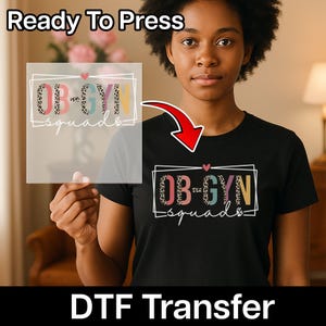 May include: Black t-shirt with the text "OB-GYN Squad" in a rectangular frame, with a heart above the text. The letters have a leopard print design. The words "Ready To Press" and "DTF Transfer" are also visible.