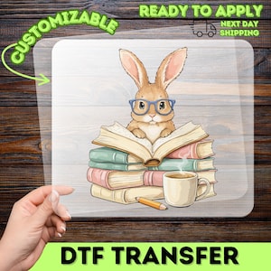 May include: A DTF transfer featuring a cartoon bunny wearing glasses, reading a book atop a stack of books. A cup of coffee and a pencil are also present. The words "CUSTOMIZABLE" and "READY TO APPLY" are visible.