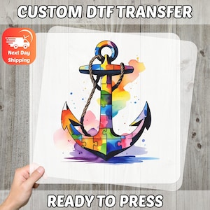 Puede incluir: Transferencia DTF lista para planchar con un diseño de ancla colorido. El ancla está compuesta por piezas de rompecabezas en colores del arcoíris, con un detalle de cuerda. Se muestra el texto "CUSTOM DTF TRANSFER" y "READY TO PRESS".
