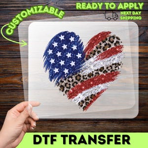 May include: A heart-shaped DTF transfer design featuring the American flag with a leopard print accent. The design includes blue stars, red stripes, and a leopard print section. The words "CUSTOMIZABLE" and "READY TO APPLY" are visible.