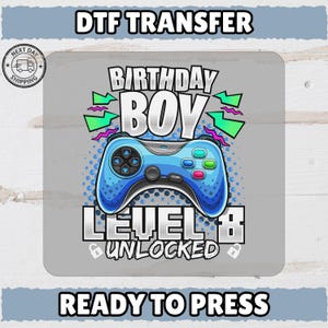 May include: A DTF transfer design featuring a blue video game controller with the words "BIRTHDAY BOY LEVEL 8 UNLOCKED". The design includes the text "READY TO PRESS" and "DTF TRANSFER".