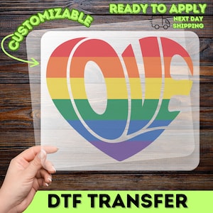 Könnte beinhalten: Eine transparente DTF-Transferfolie mit einer großen herzförmigen Grafik, in der das Wort LOVE steht. Das Design ist mit horizontalen Streifen in den Farben Rot, Orange, Gelb, Grün, Blau und Violett gefüllt, die einen Regenbogeneffekt erzeugen.