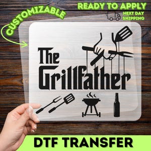 May include: A black DTF transfer featuring the text "The Grillfather" and barbecue-themed illustrations. The design includes a grill, utensils, and a beer bottle. The transfer is displayed against a wooden backdrop.