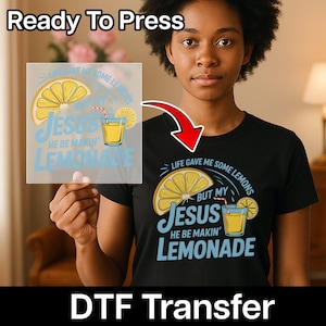 Puede incluir: Una camiseta negra con un gráfico que dice "Life gave me some lemons but my Jesus he be makin' lemonade". El diseño incluye una rodaja de limón y un vaso de limonada. También se ven las palabras "Ready To Press" y "DTF Transfer".