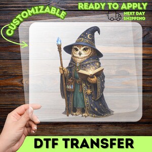 May include: A DTF transfer sheet featuring a graphic illustration of an owl dressed as a wizard. The owl wears a dark blue star-patterned robe and pointed hat, holding a wooden staff with a blue crystal and an open glowing book.