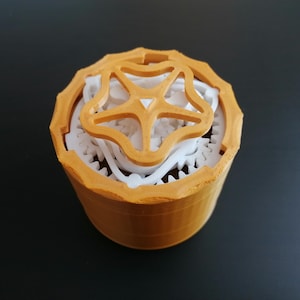 May include: A 3D printed, orange and white, gear-shaped box with a decorative, star-shaped lid.