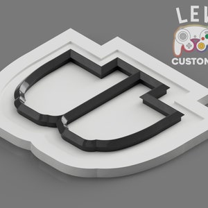 May include: A white plastic mold with a black cutout in the shape of the letter "U". The mold is designed for creating custom controller buttons for the Nintendo GameCube.