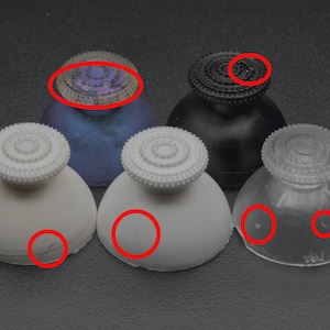 Puede incluir: Colección de cinco tapones decorativos para botellas. Los tapones tienen una base redondeada y una parte superior circular detallada. Los colores incluyen blanco, negro, transparente y un azul iridiscente. Los tapones son probablemente para vino u otras botellas.