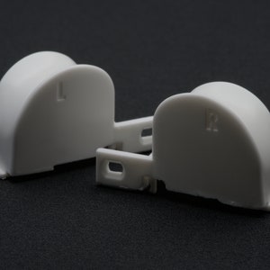 May include: Two white plastic end caps for a light fixture. The left end cap has the letter "L" printed on it and the right end cap has the letter "R" printed on it.