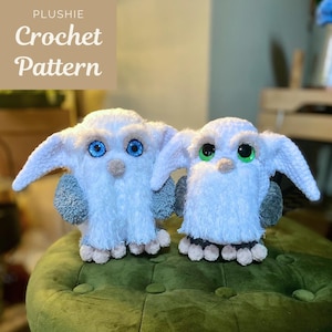 May include: Two white plushie owl toys with large eyes, one with blue eyes and the other with green eyes. The owls have grey wings and beige feet. The text "PLUSHIE Crochet Pattern" is in the upper left corner.