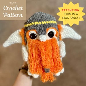 Könnte beinhalten: Handgefertigte Zwergenpuppe aus Häkelarbeit mit grau-gelbem Hut, orangefarbenem Bart und großen schwarzen Augen. Die Puppe hat weiße Flügel und der Text "Crochet Pattern" ist sichtbar. Ein gelber Stern weist auf "ATTENTION: THIS IS A MOD ONLY!"