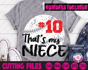 May include: A gray t-shirt with a white baseball graphic and the text "That's my niece #10". The text is in black. The number 10 is in red. The shirt is on a wooden surface with a pair of white sneakers and blue jeans.