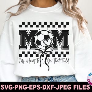 May include: White sweatshirt with a black and white graphic design. The graphic features a soccer ball with a heart, the word "MOM" and the text "My Heart Is On That Field".