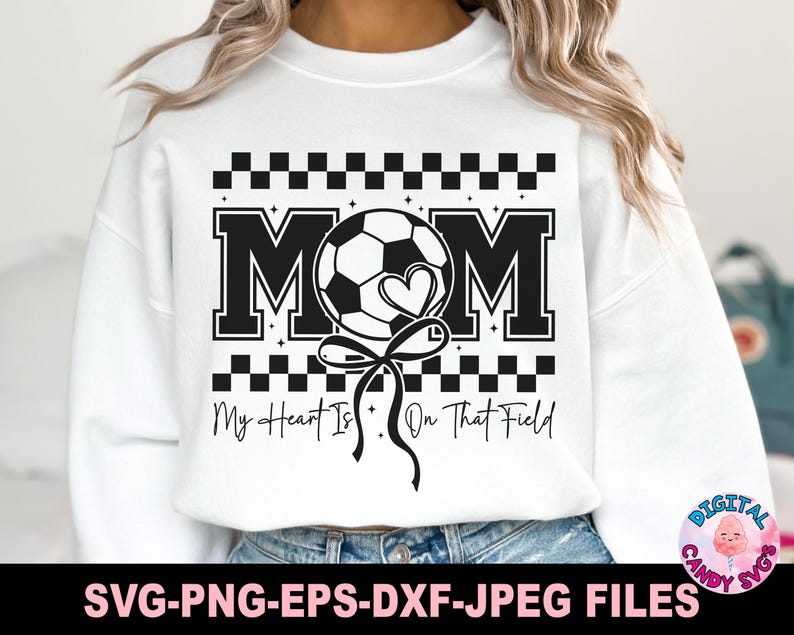 May include: White sweatshirt with a black and white graphic design. The graphic features a soccer ball with a heart, the word "MOM" and the text "My Heart Is On That Field".