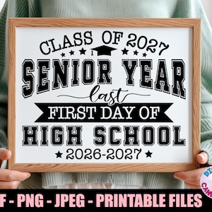 May include: A framed sign with the text "CLASS OF 2027 SENIOR YEAR last FIRST DAY OF HIGH SCHOOL 2026-2027". The sign is in a wooden frame and held by a person. The sign is black and white.